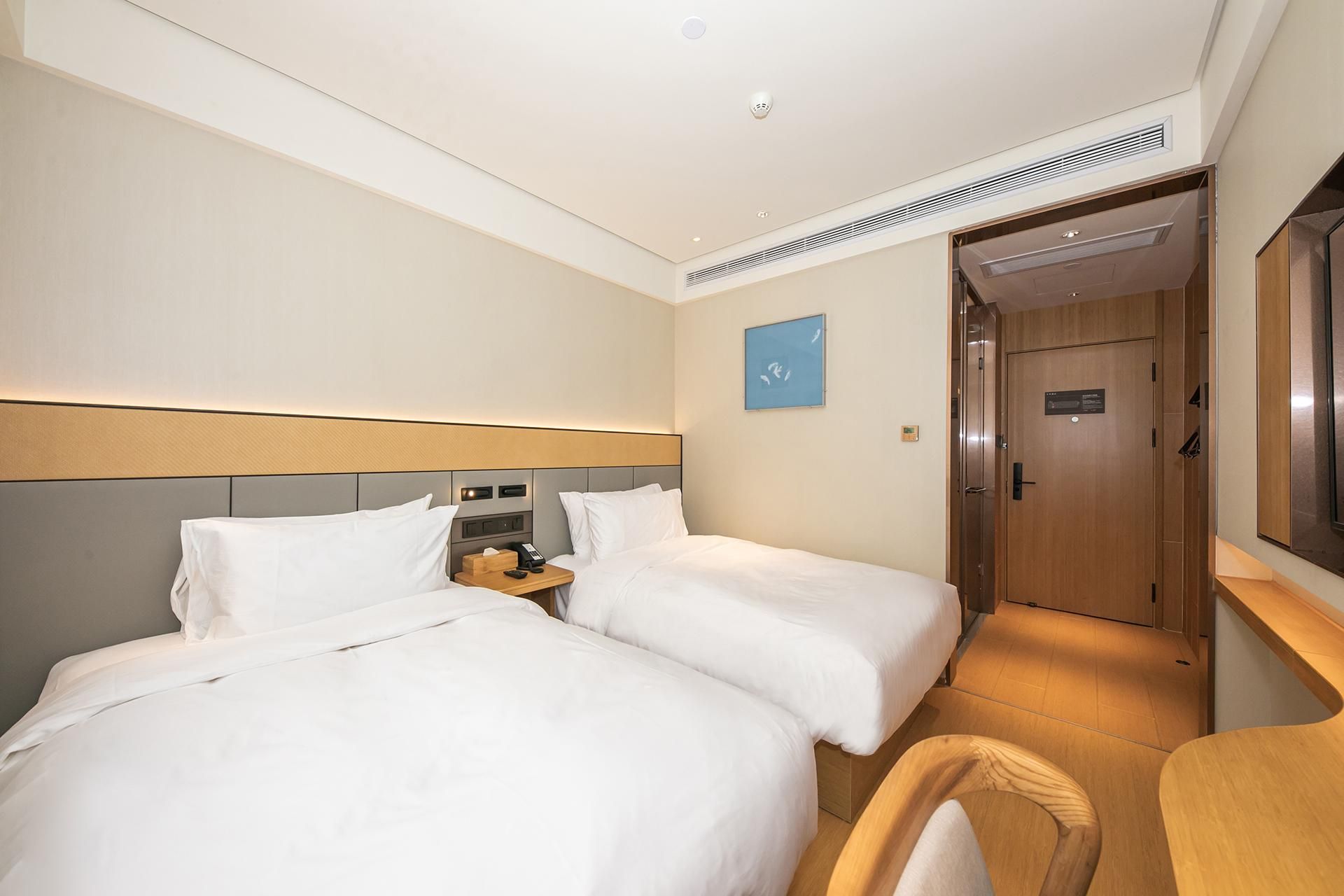 Habitació d'hotel amb dos llits, un escriptori, una cadira, una tauleta de nit i una porta.