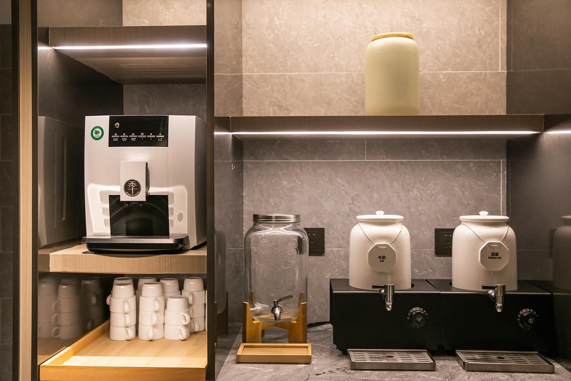 Una estación de café con una máquina de café, una jarra de vidrio y dos dispensadores de leche.