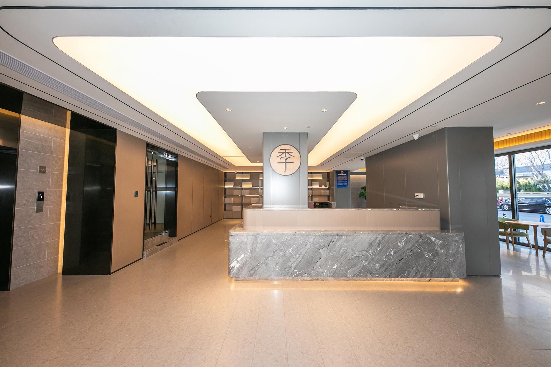 A modern lobby with a marble reception desk, elevators, and a large window with a view of the street.