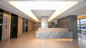 A modern lobby with a marble reception desk, elevators, and a large window with a view of the street.