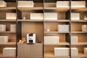 Un interior moderno con varias estanterías llenas de libros y objetos decorativos, una cafetera y una pequeña mesa con una caja de pañuelos y una taza.