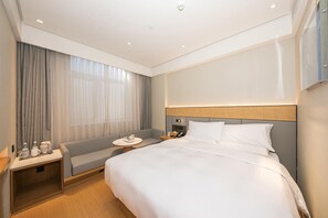 A hotel room with a large bed, a bedside table with a lamp, a small seating area, and a large window with curtains. - Ji Hotel Beijing Sanlitun Taikoo Li (Beijing)