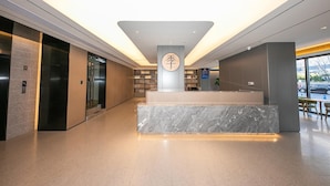 A modern lobby with a marble reception desk, elevators, and a large window with a view of the street.