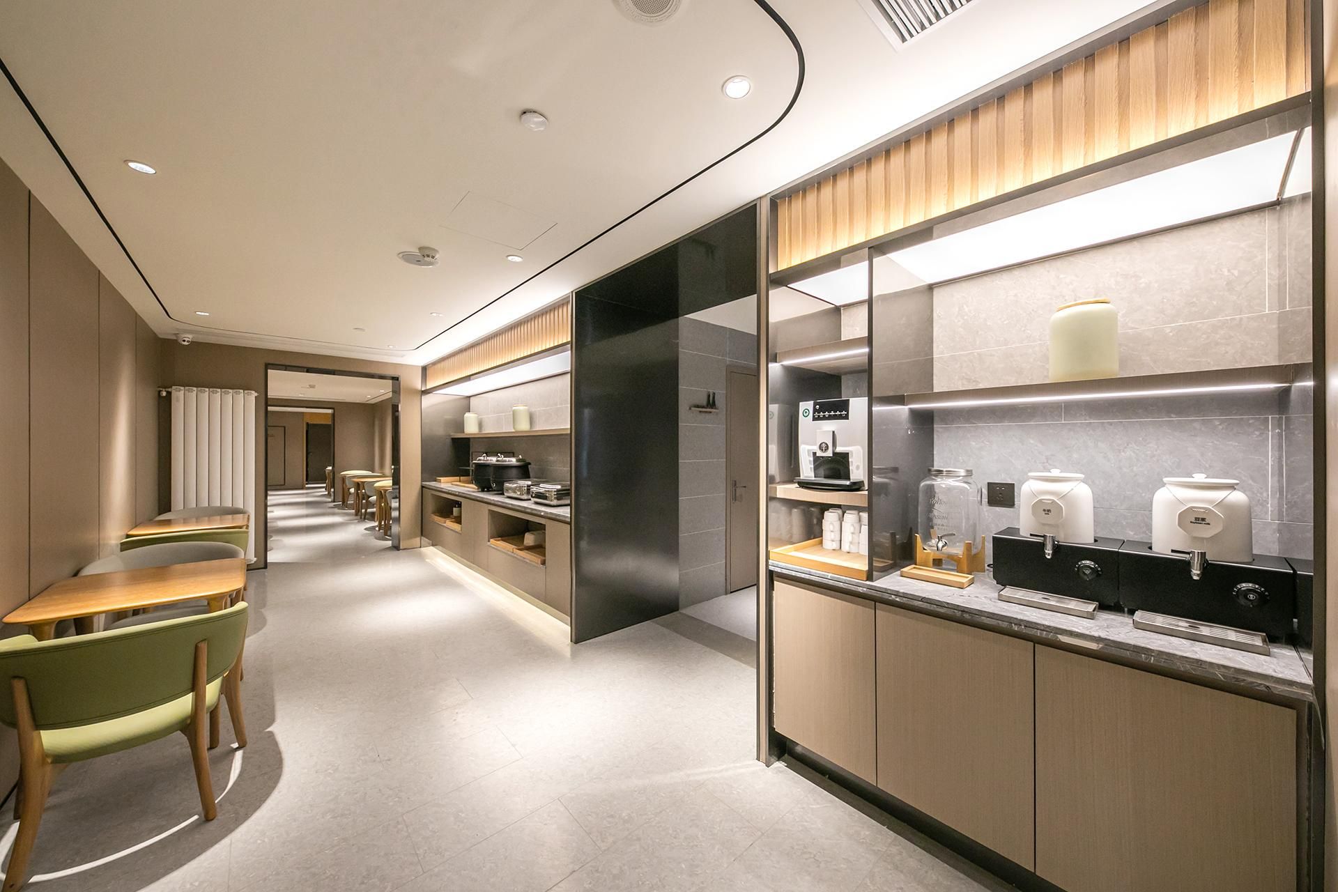 A modern hotel lobby with a long corridor, seating area, and a kitchenette with coffee machines.