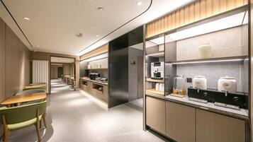 A modern hotel lobby with a long corridor, seating area, and a kitchenette with coffee machines.