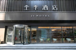 Entrada de un hotel con puerta giratoria, grandes ventanales y un letrero que dice 'JI HOTEL'.