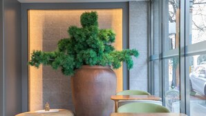 A modern interior with a large potted plant, a wooden sculpture, and a seating area with a table and chairs.