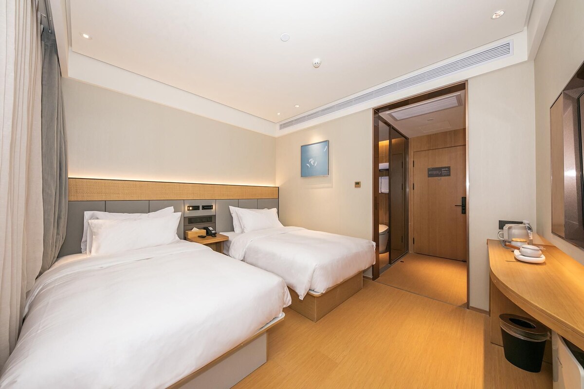 Habitación de hotel con dos camas, una mesita de noche con un teléfono, un escritorio pequeño con una cafetera y una puerta que da a un baño.