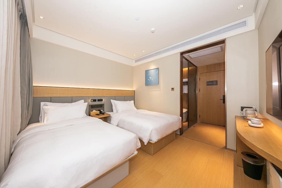 Ein Hotelzimmer mit zwei Betten, einem Schreibtisch, einem Spiegel und einer Tür zu einem Badezimmer.