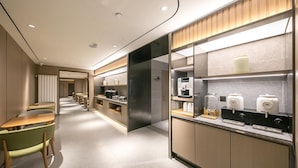 A modern hotel lobby with a long corridor, seating area, and a kitchenette with coffee machines.