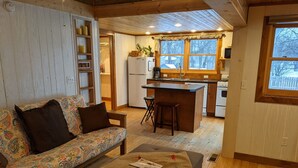 A cozy cabin interior with a sofa, ottoman, and a kitchen area including a refrigerator, sink, and bar stool. - Arnolds Park Cabin with kayaks, bikes, and golf cart (Arnolds Park)
