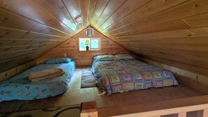 A cozy attic bedroom with two beds, a window with a lamp, and a wooden ceiling. - Arnolds Park Cabin with kayaks, bikes, and golf cart (Arnolds Park)