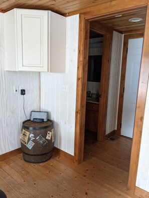 Una habitación con suelo de madera, una puerta blanca y un barril de madera con pegatinas.