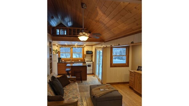 A cozy cabin interior with a wooden ceiling, a dining area, a kitchen, and a living room with a sofa and ottoman. - Arnolds Park Cabin with kayaks, bikes, and golf cart (Arnolds Park)