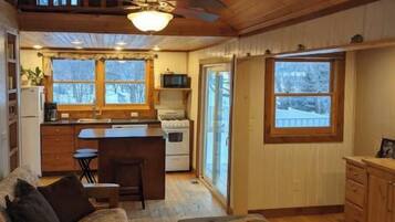A cozy cabin interior with a wooden ceiling, a dining area, a kitchen, and a living room with a sofa and ottoman.