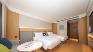 Une chambre d’hôtel moderne avec deux lits, une petite table ronde sur laquelle se trouvent une tasse et une soucoupe, et un plancher en bois.