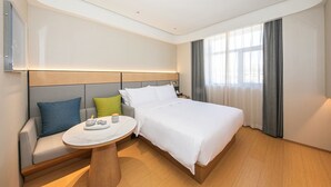 Une chambre d’hôtel moderne, dotée d’un grand lit, d’un canapé, d’une petite table ronde et d’une grande fenêtre avec des rideaux.