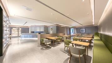A modern dining area with multiple tables and chairs, a reception desk, and a counter with a logo.