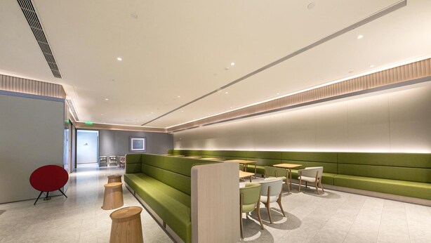 Un espace d’attente moderne avec des sièges verts, des tables en bois et un fauteuil rouge.