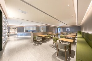 A modern dining area with multiple tables and chairs, a reception desk, and a counter with a logo. - Ji Hotel (Beijing)