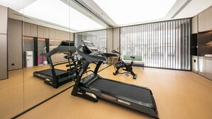 Une salle de sport moderne équipée de tapis de course, de vélos d’appartement et d’un mur recouvert de miroirs.