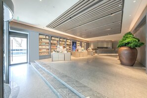 A modern interior with a reception desk, shelves with books, and a large potted plant. - Ji Hotel (Beijing)