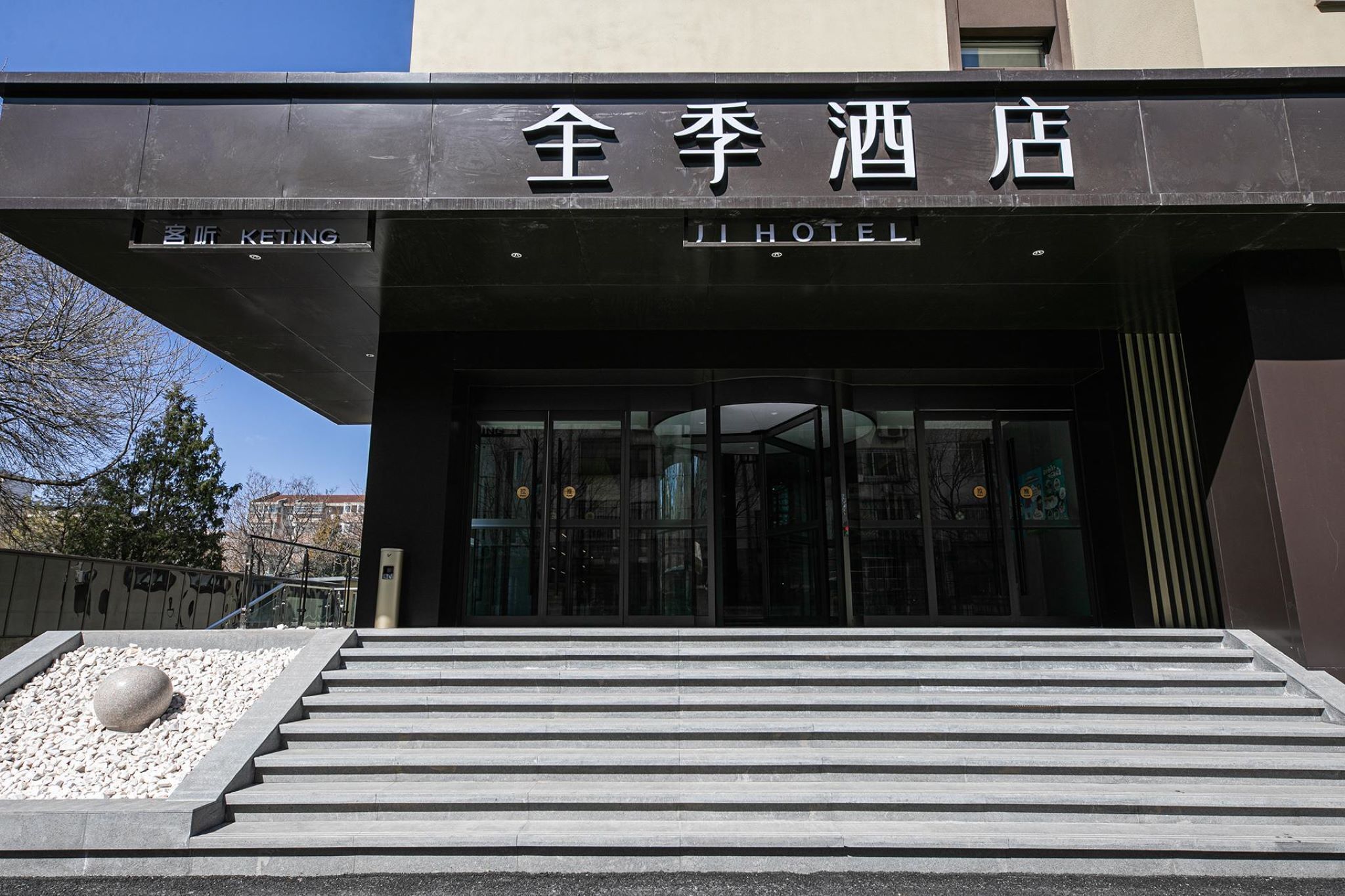 L’entrée de l’hôtel Ji présente un design moderne, avec une façade en verre et un escalier menant à l’entrée.
