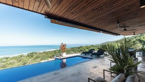 Una piscina infinita amb vistes a l'oceà, envoltada de gandules i plantes en testos.