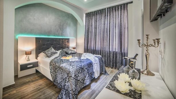 A modern bedroom with a large bed, a nightstand, a wall-mounted TV, and a decorative candelabra. - Hotel Boutique Natka (Rovinj)
