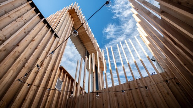 A wooden structure with vertical beams and string lights, viewed from below.