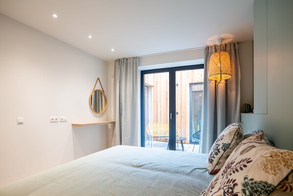 A bedroom with a bed, a mirror, a window with curtains, and a ceiling light.