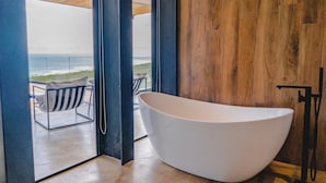 A modern bathroom with a large white bathtub, wooden paneling, and a view of the ocean through an open door. - Ocean View Casa Nina, Santa Teresa - 2 Bedrooms! (Santa Teresa)