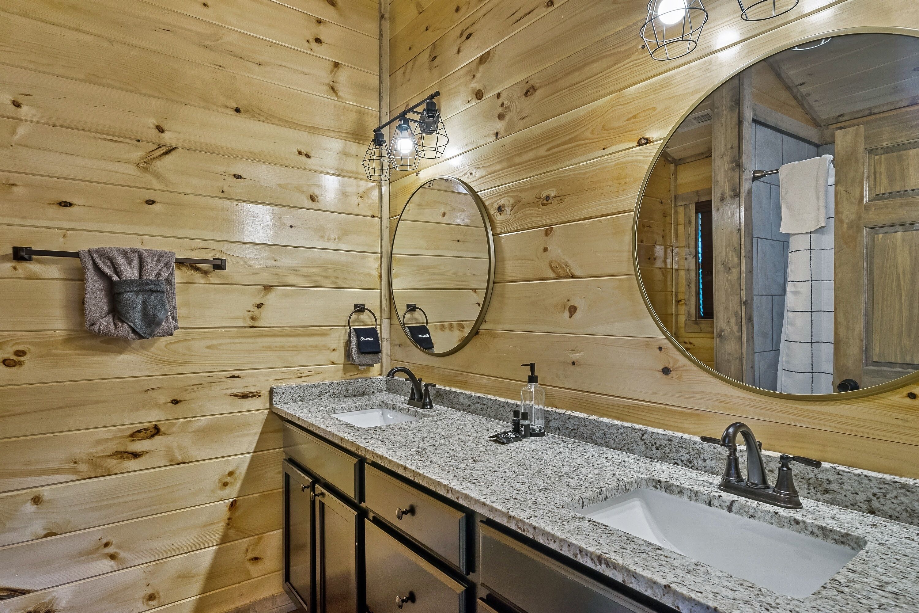 A wooden-paneled bathroom with two sinks, a large mirror, and a towel rack.