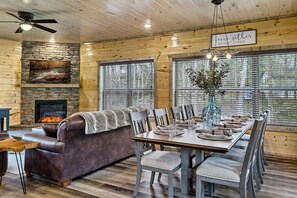 A cozy cabin interior with a stone fireplace, a dining table set for four, and a leather sofa.