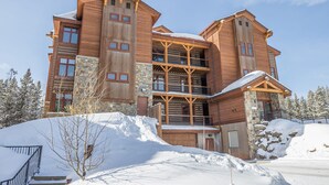Una cabaña de madera de varios pisos con balcones y fachada de piedra, rodeada de nieve.
