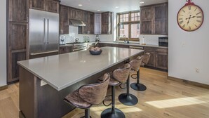 Una cocina moderna con armarios de madera oscura, electrodomésticos de acero inoxidable, una isla grande con taburetes de bar y un reloj montado en la pared.