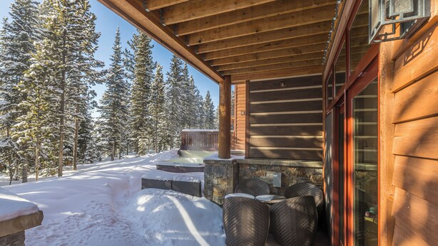 Una cabaña de madera con chimenea de piedra, mobiliario exterior y un paisaje cubierto de nieve.