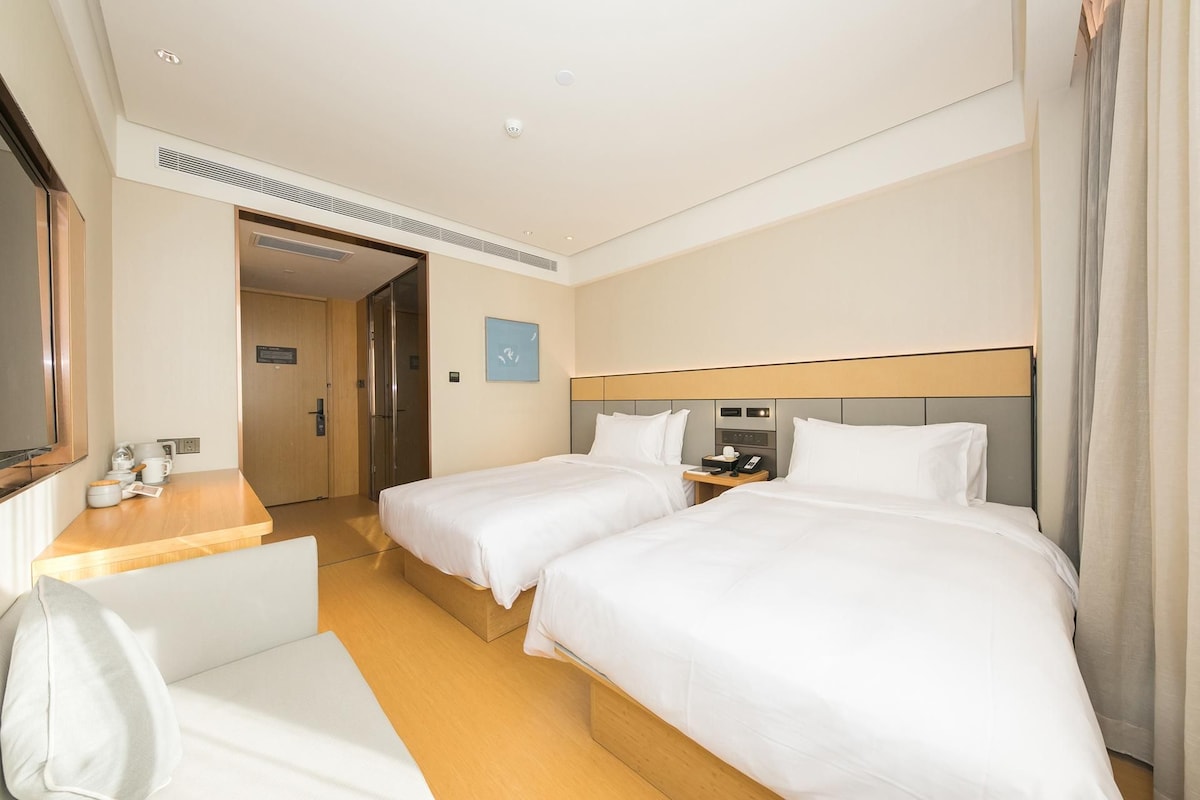 A hotel room with two beds, a desk, a chair, and a bathroom door.