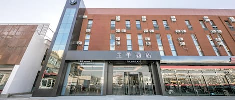 A hotel with a modern facade, large glass entrance, and multiple air conditioning units.