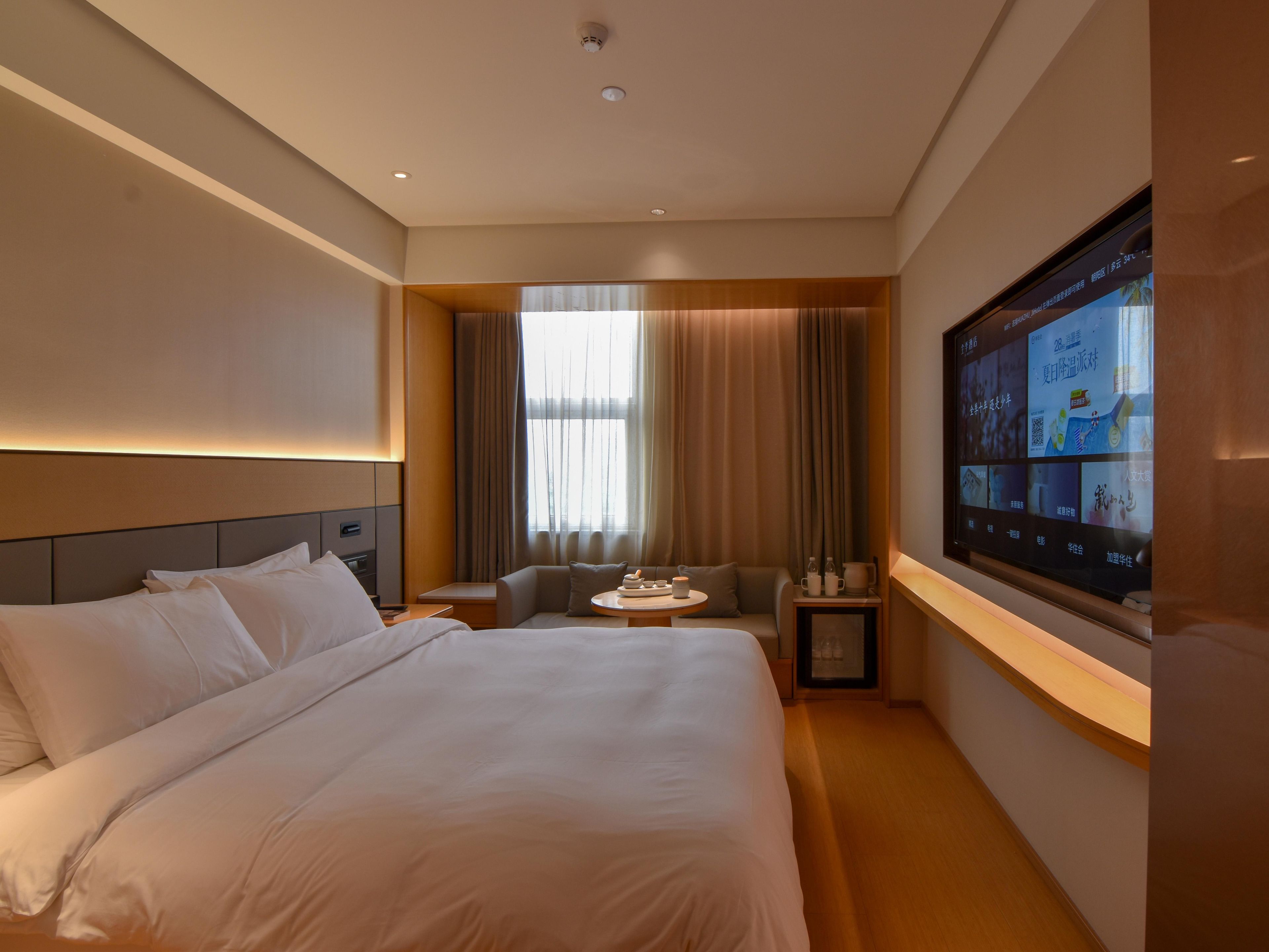 Quarto de hotel com uma cama grande, área de estar com mesa e televis ão exibindo conteúdo.