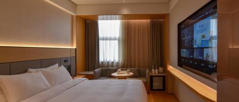 A hotel room with a large bed, a seating area with a table, and a television screen displaying content.