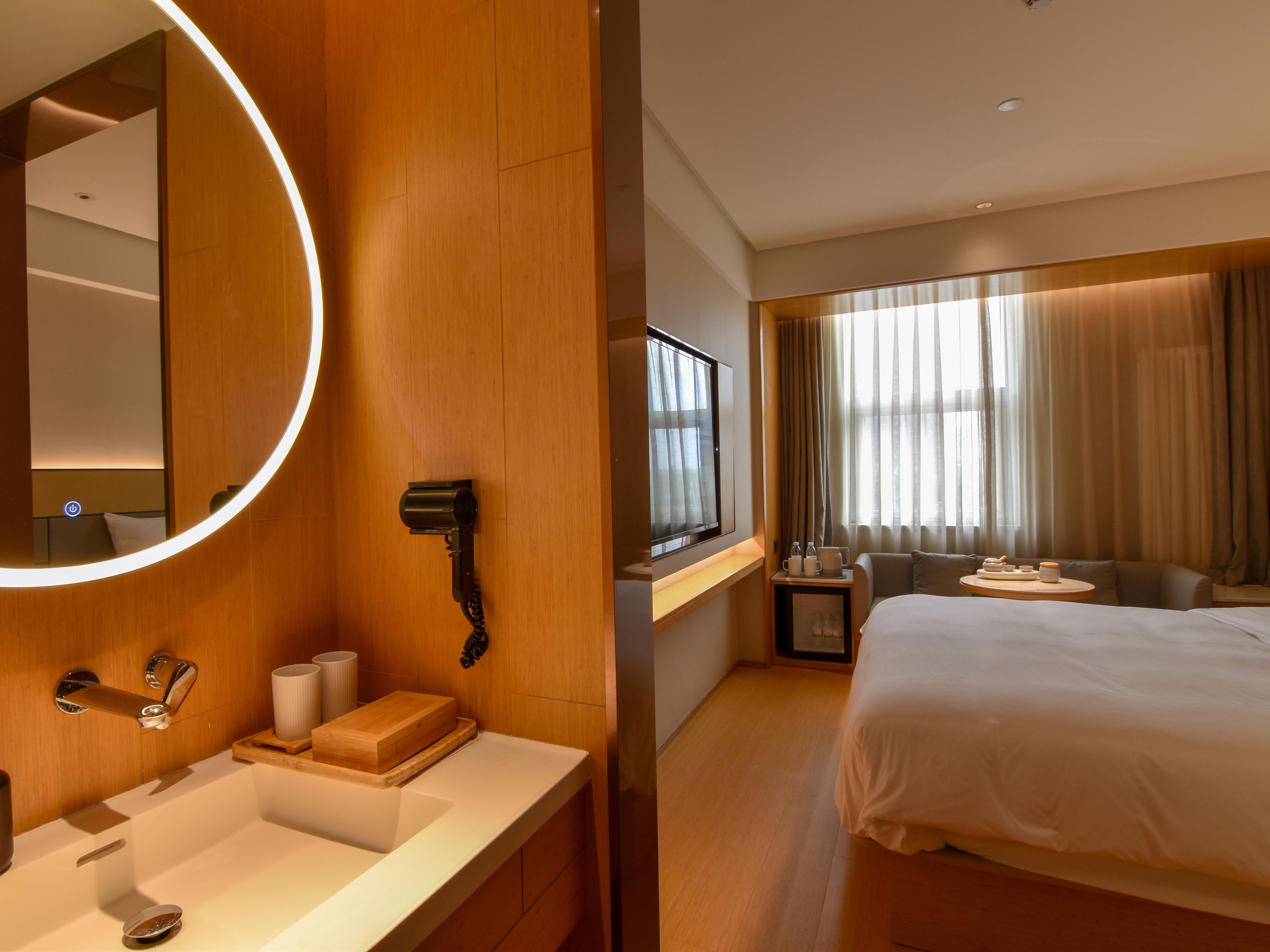 Ein Hotelzimmer mit einem großen Bett, einem runden Spiegel, einem Schminktisch mit Waschbecken und einem Fernseher.