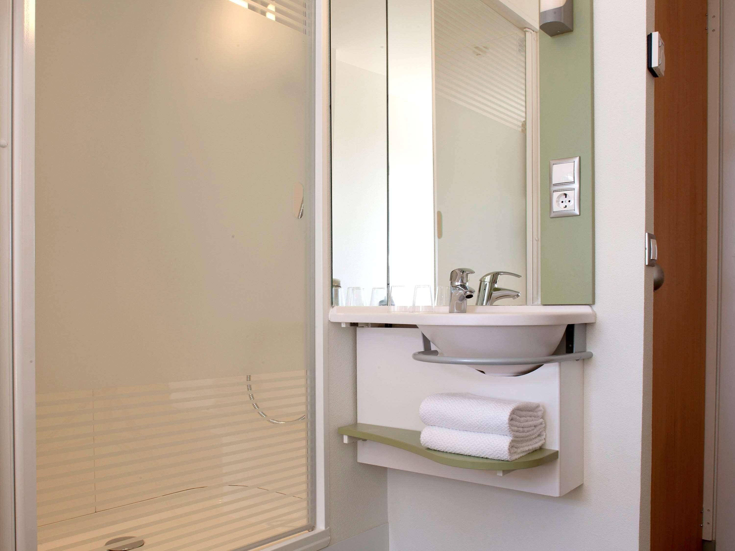 A bathroom with a shower, a sink, a mirror, and a towel rack.
