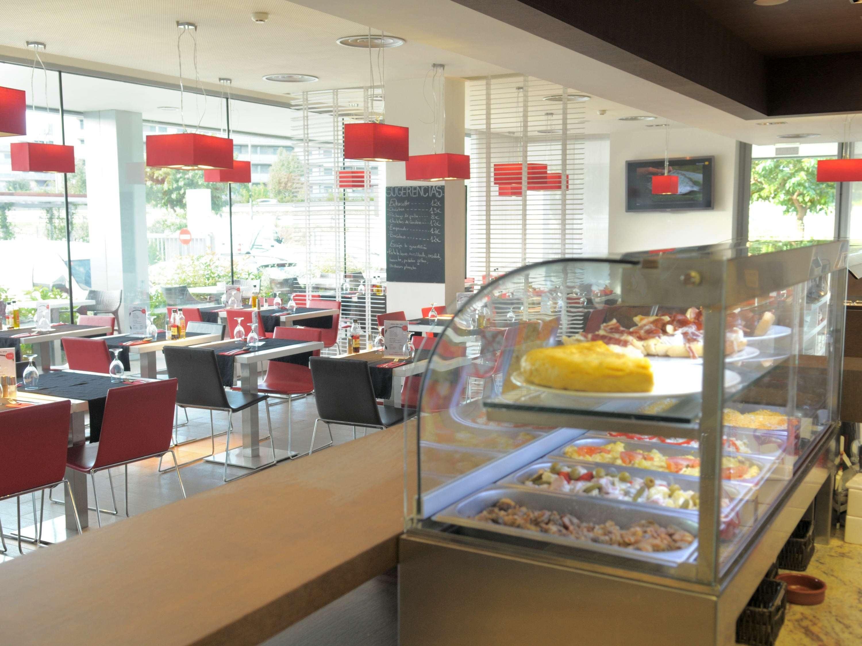 Un restaurante moderno con divisiones de vidrio, sillas rojas y una pizarra con el menú.
