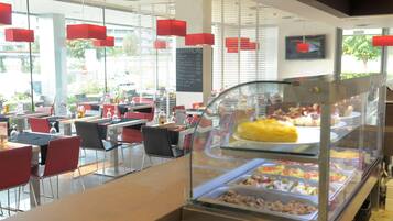 Un restaurante moderno con divisiones de vidrio, sillas rojas y una pizarra con el menú.