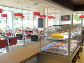 Un restaurante moderno con divisiones de vidrio, sillas rojas y una pizarra con el menú.