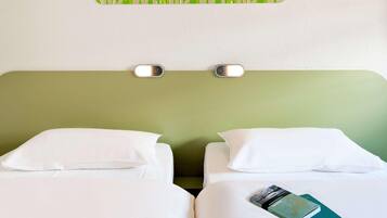 Ein Hotelzimmer mit zwei Betten, weißer Bettwäsche, einem grünen Kopfteil und einer wandmontierten Lampe.