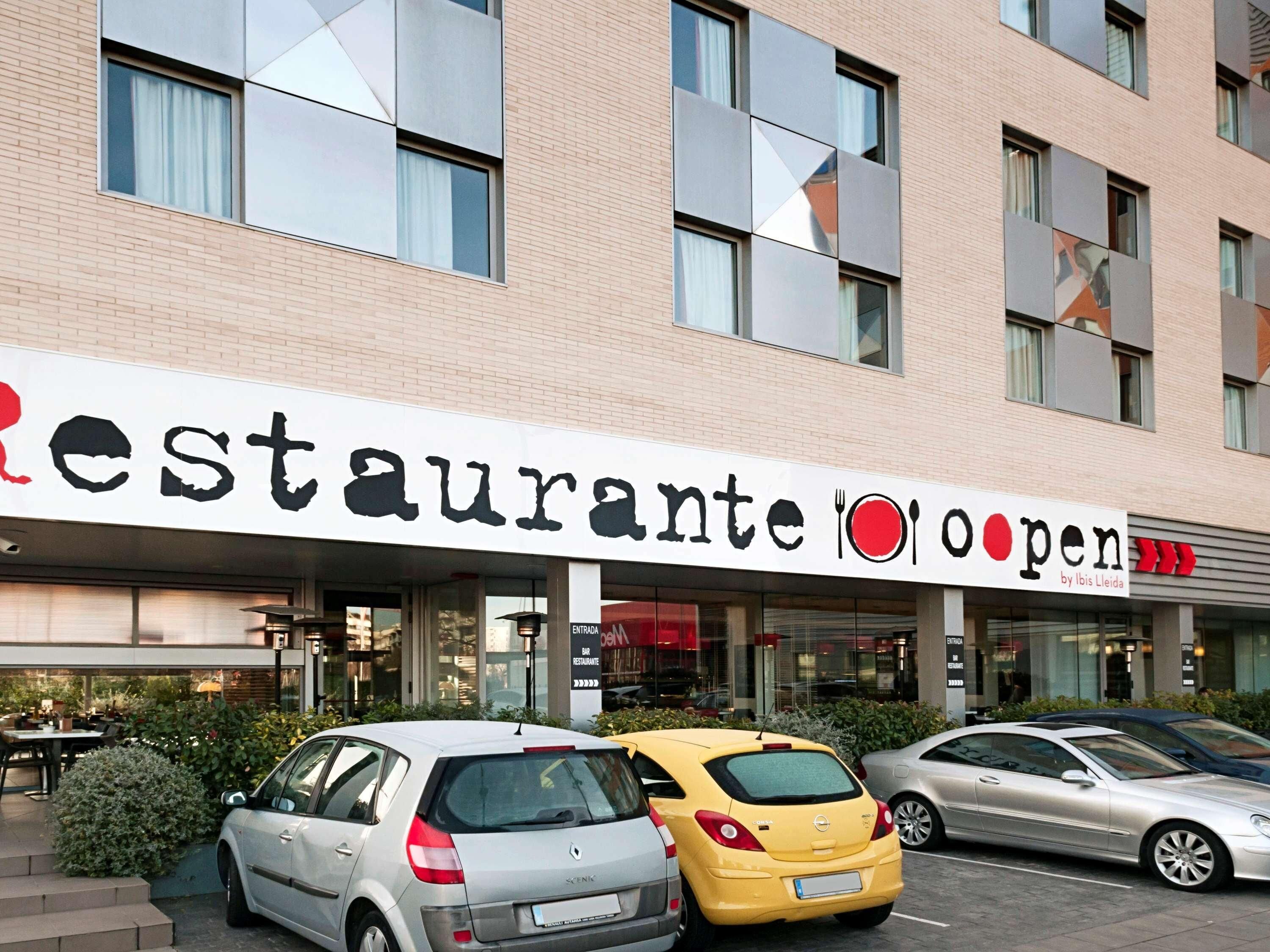 A building with a sign reading 'Restaurante Open' and a car parked in front.