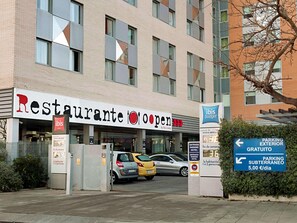 Un restaurante con un letrero que indica 'ibis budget' y que está 'abierto'. Hay coches estacionados delante y se ve un letrero que dice 'PARKING EXTERIOR GRATUITO'.