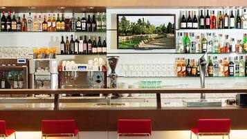 Zona de bar con diversas botellas de licor, una máquina de café y una pantalla de televisión mostrando un paisaje.